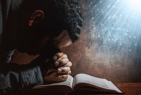 man-resting-head-on-praying-hands-on-open-bib